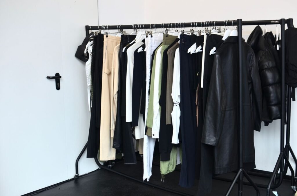 Collection of stylish clothes and outerwear on hangers hanging on rack near door in light wardrobe room in modern studio